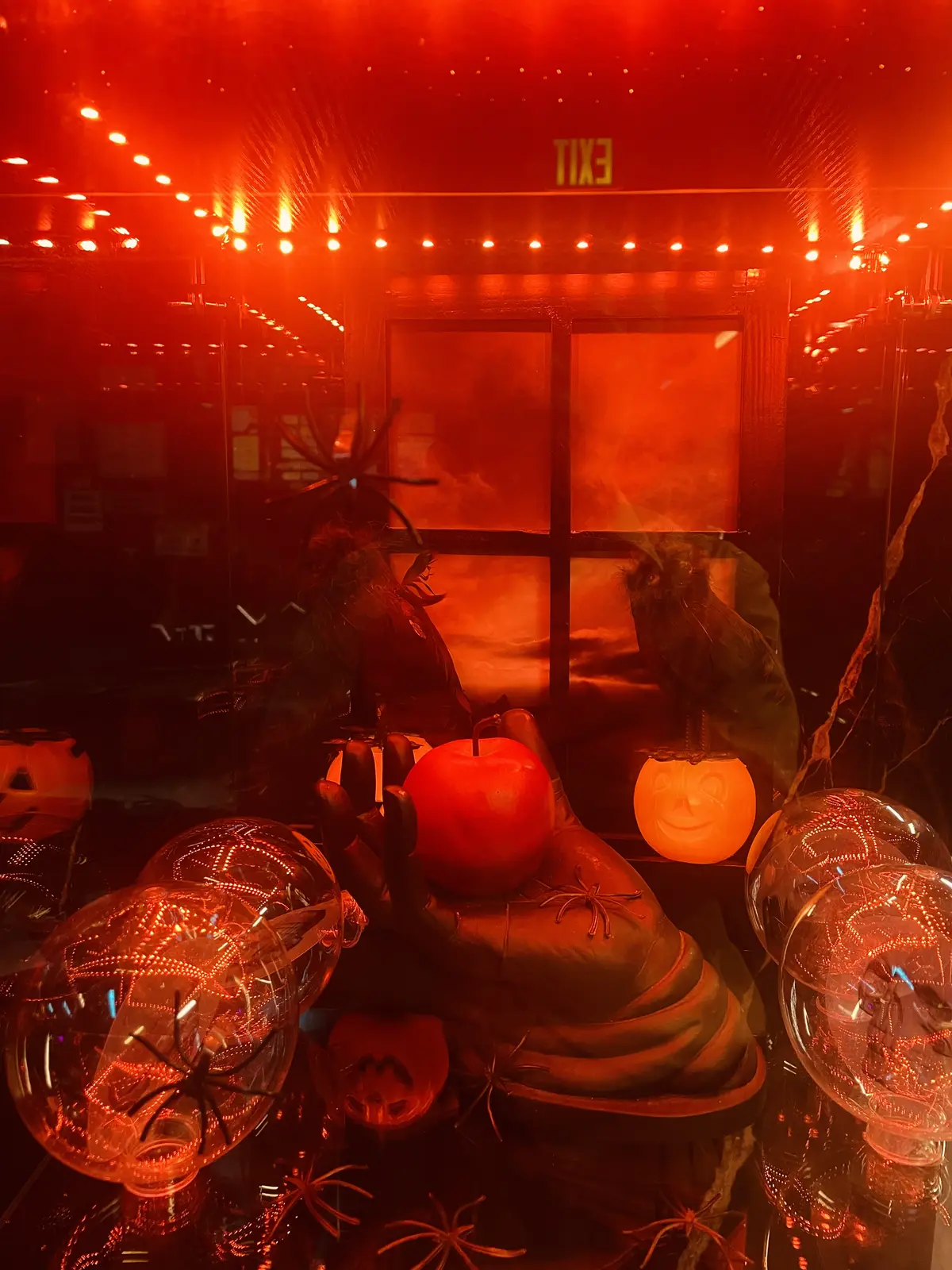 Orange-lit haunted window display with pumpkins and glass skulls